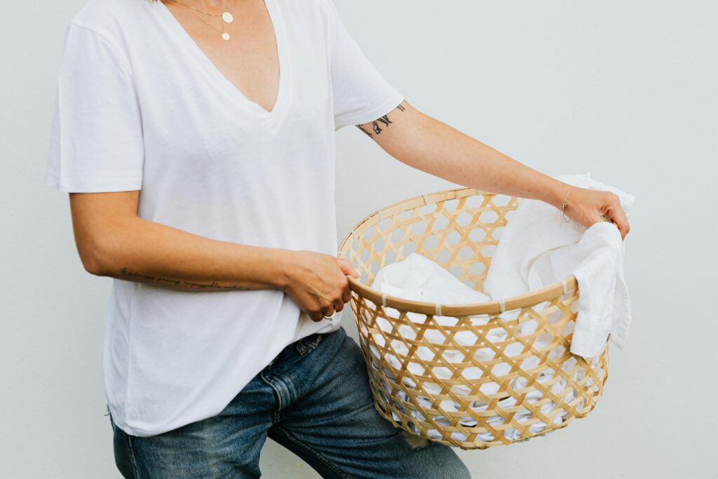 Woman placing laundry into a woven basket in a calm, neutral home.