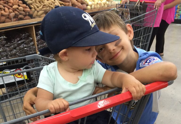Two young children riding together in a grocery cart during an ordinary family shopping trip